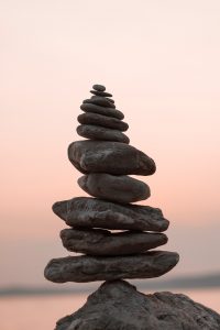 A tall stack of smooth, flat stones balanced on top of one another against a soft pastel sky, creating a calm scene.