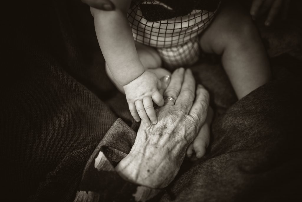 a hand of an elder being touched by a hand of a young child.
