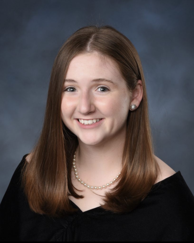 A female student smiling, wearing a black shirt and pearl necklace.